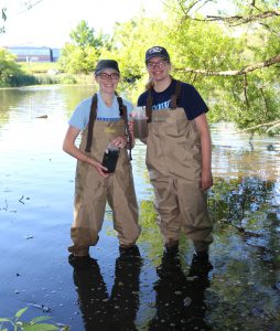 Two Etown students stand in Lake Placida, holding samples they collected.