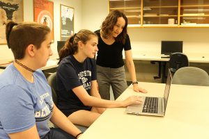 Two Etown students and professor viewing laptop in classroom.