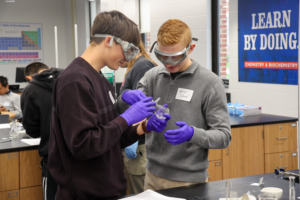Two students huddle over a chemistry flask.